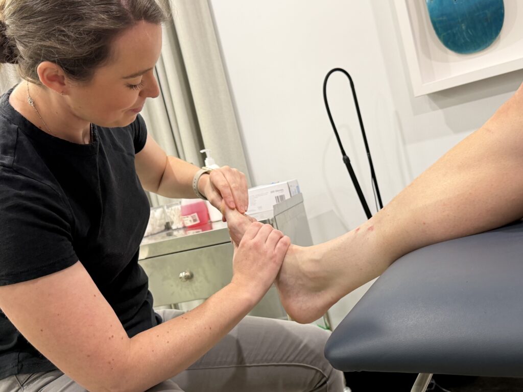 Podiatrist performing a clinical assessment for big toe arthritis by examining joint movement and pain response.